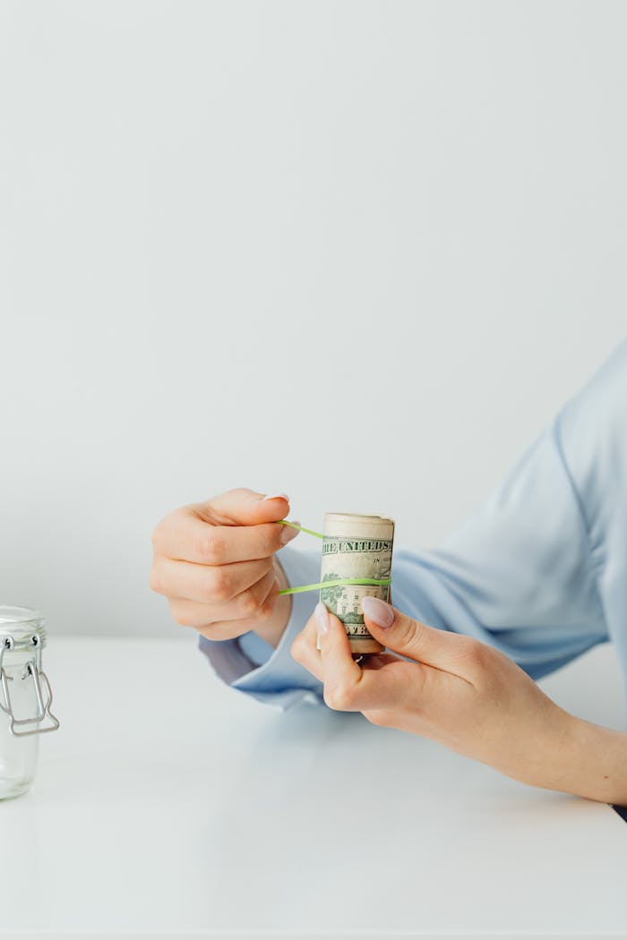 Close-up of hands securing a roll of US dollar bills with a rubber band on a white desk.